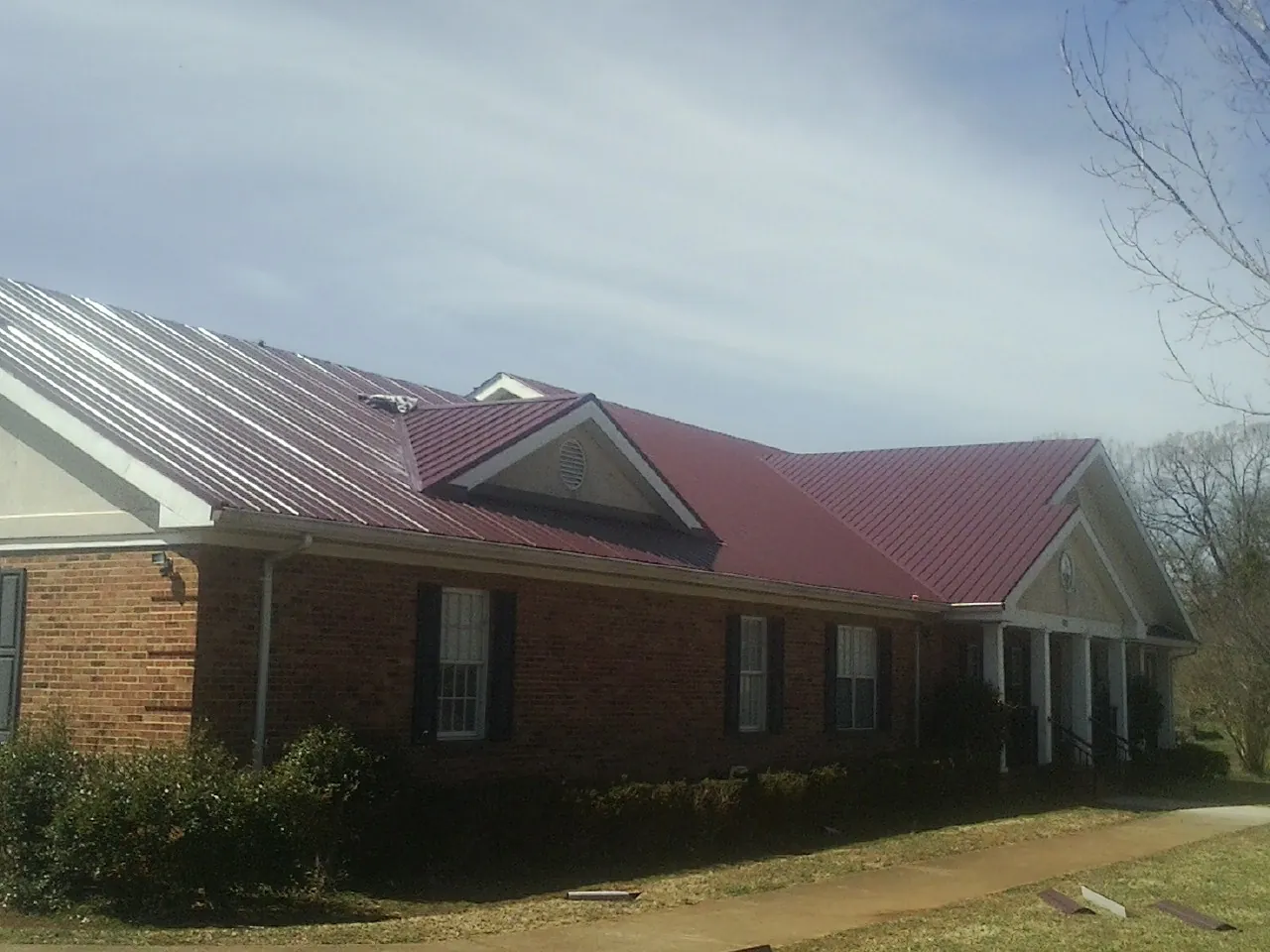 Red metal roof with gabled entries on a long brick building, from a Hail Damage Roof Repair job in Port Barre