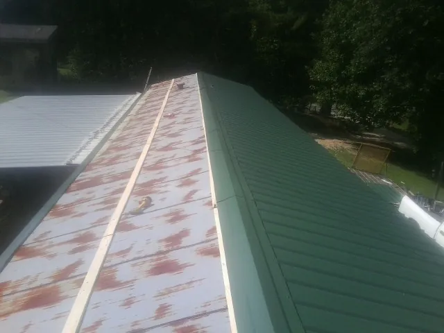 Old rusted panels beside newly installed green metal roofing — Wind Damage Roof Repair by Roofing Brothers in Port Barre