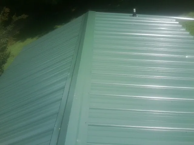 New green metal panels meeting at the ridge of a roof — Flat Roof Repair work by our crew in Port Barre