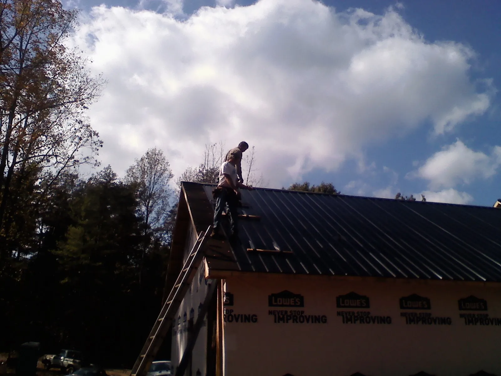 Roofer fastening dark metal panels high against a cloudy sky, from a Roof Inspection job in Port Barre