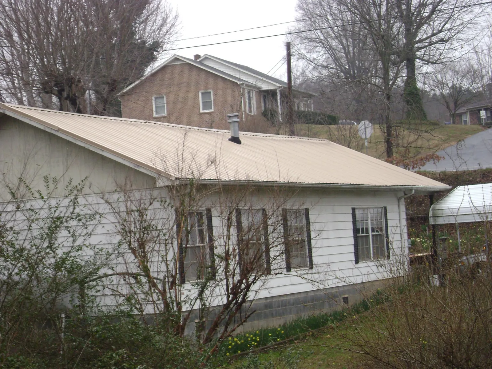 Tan metal roof on a white sided house set into a hillside — Commercial Roofing by Roofing Brothers in Port Barre