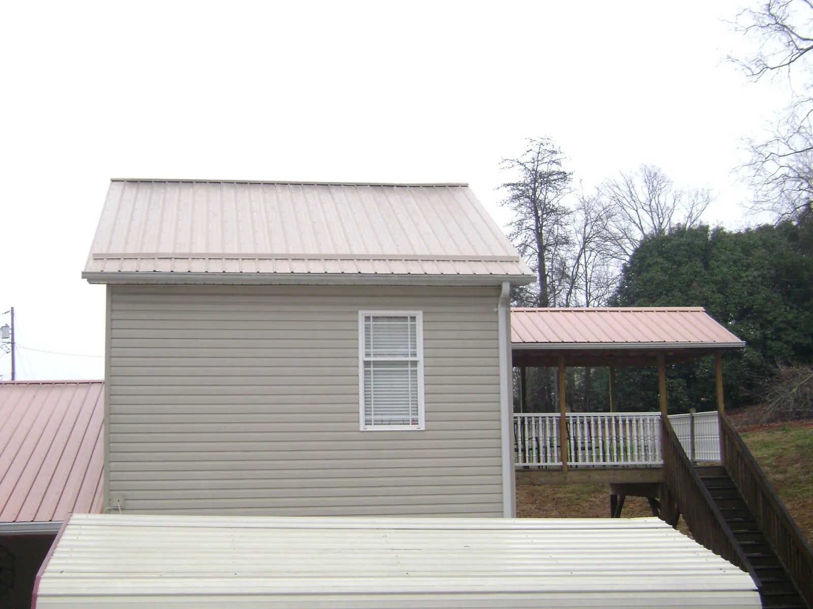 Tan metal roofs on a two story addition and attached porch, from a Roof Replacement job in Port Barre